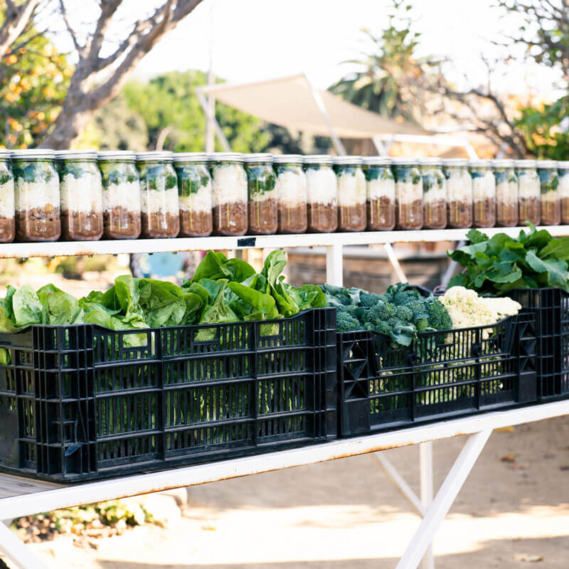 Metal cart loaded with healthy pre-made meals in glass jars and fresh produce.
