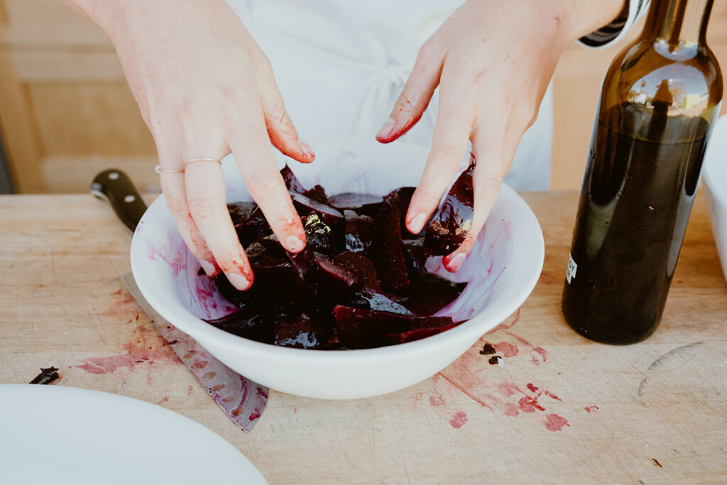 Removing beets skin by hand in a bowl and mixing with olive oil.