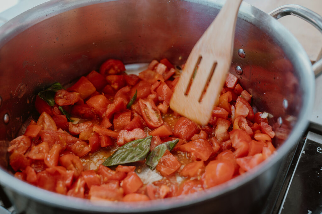Chunks of San Marzano tomatoes mixed with basil in a large pot.