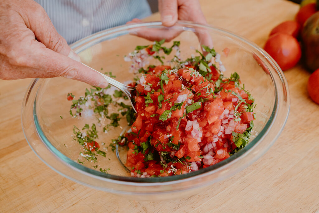 Simple tomato salsa being mixed in clear bowl.