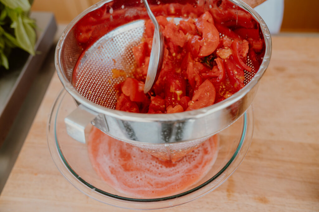 Blended tomatoes being strained over large bowl to collect juice.
