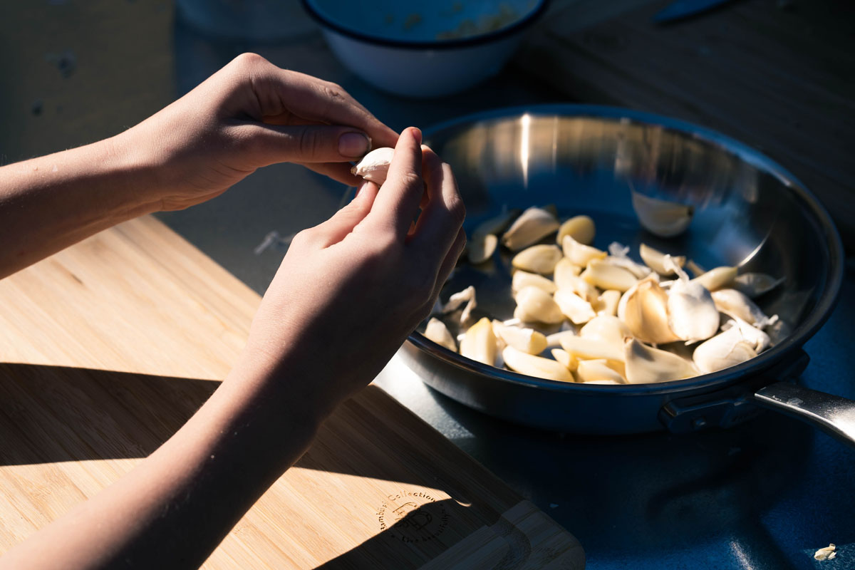Close up of hands peeling garlic into a bowl.