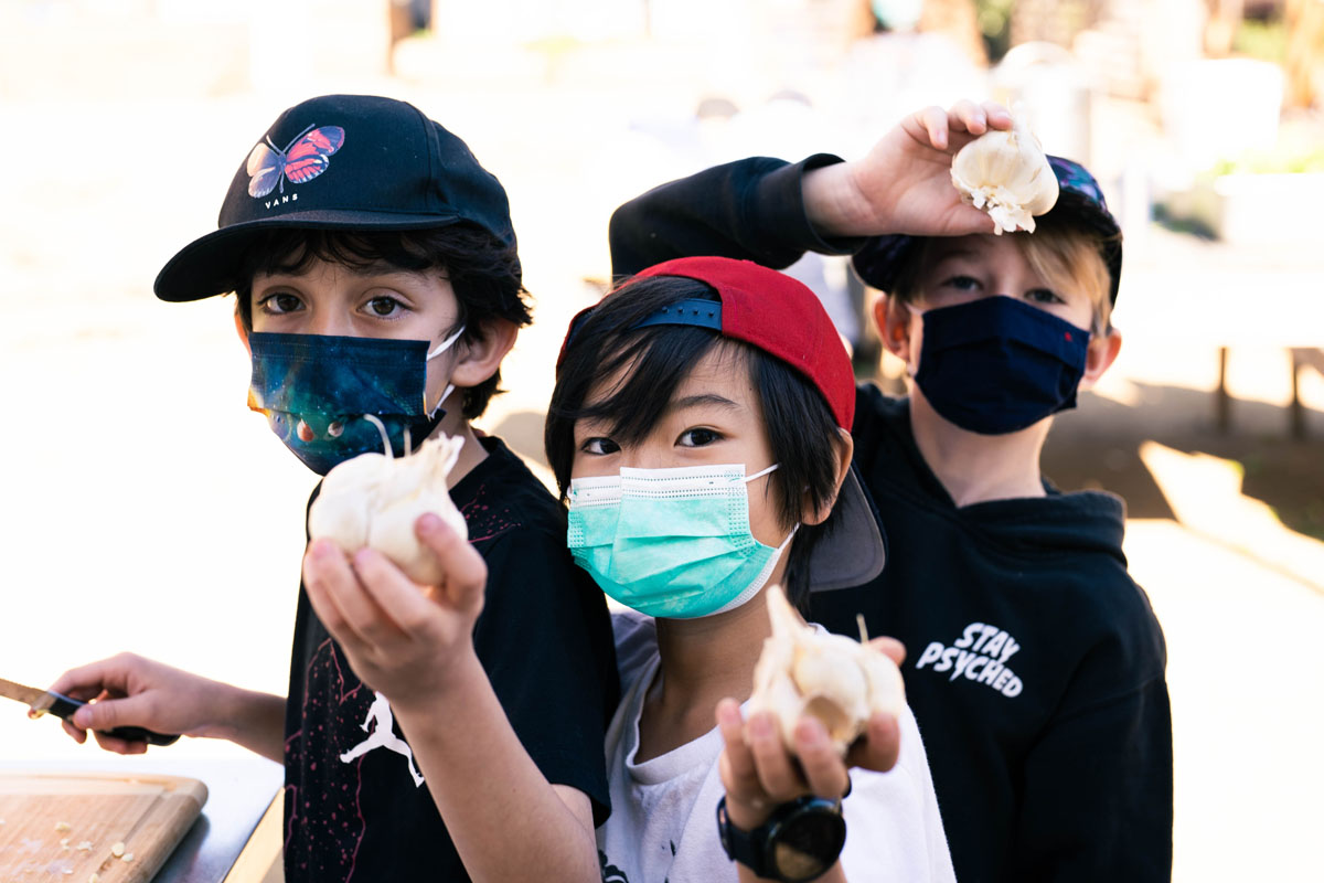 Children wearing masks hold up fresh produce.
