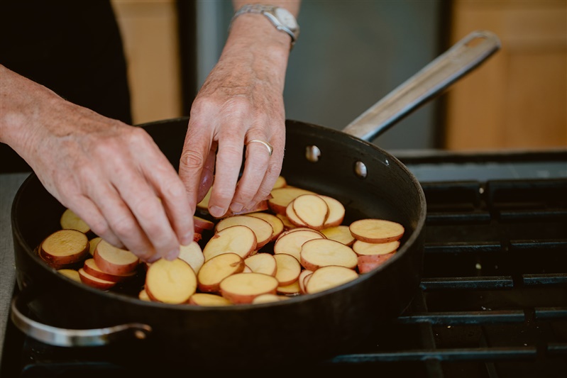 Hands placing Yukon potatoes in large saute pan over stove.