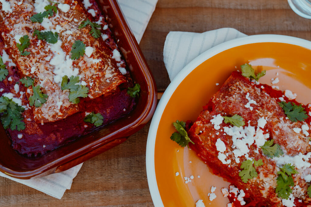 Top down shot of butternut squash enchiladas on plate and in a baking dish.