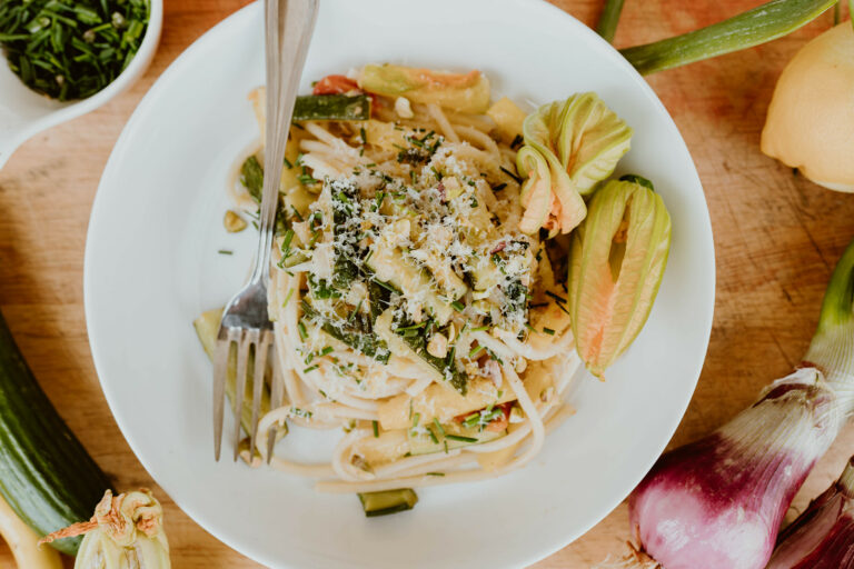 Summer squash pasta on a plate with fork and ingredients surrounding it.