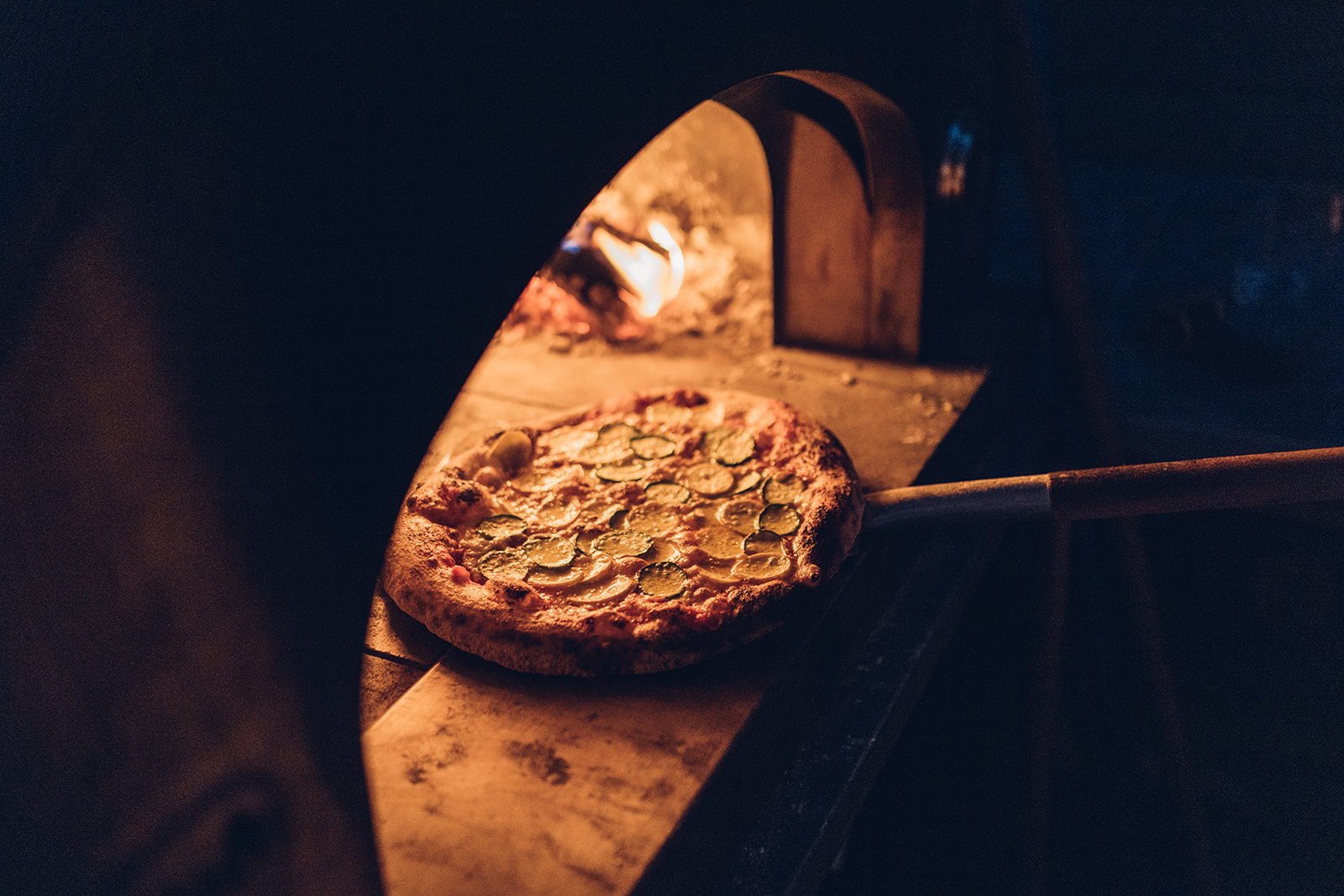 Pizza being pulled out of wood burning oven.