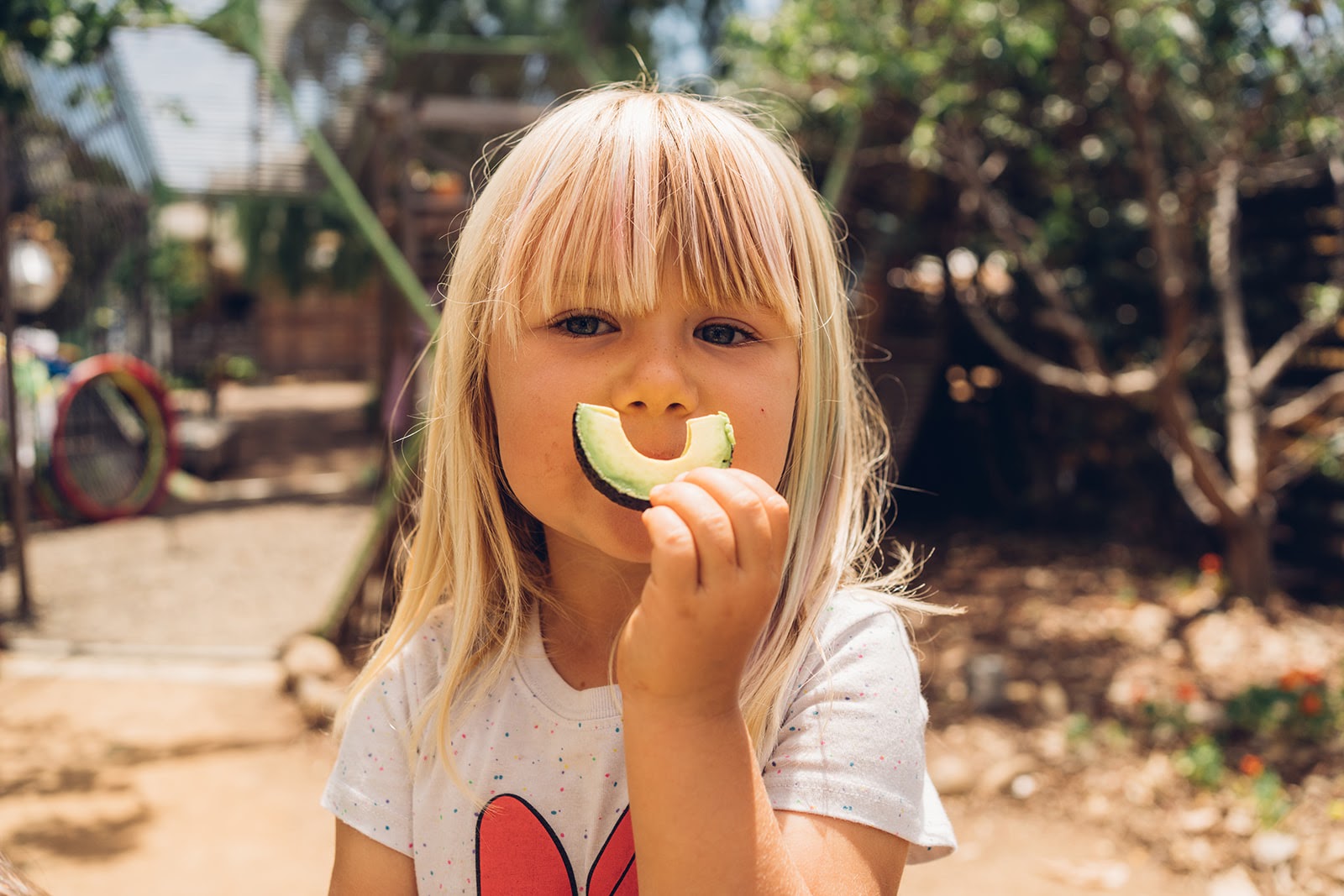 Child holding avocado slice near face