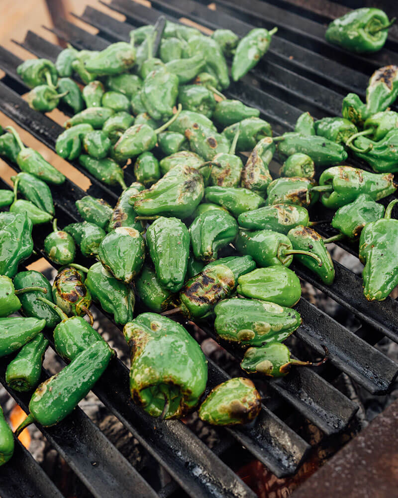 Green peppers being roast over open fire on a grill.