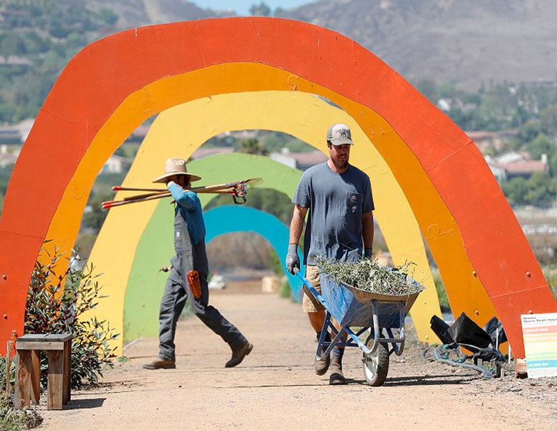 Person walks a wheel barrow through the rainbow arches on The Ecology Center farm.
